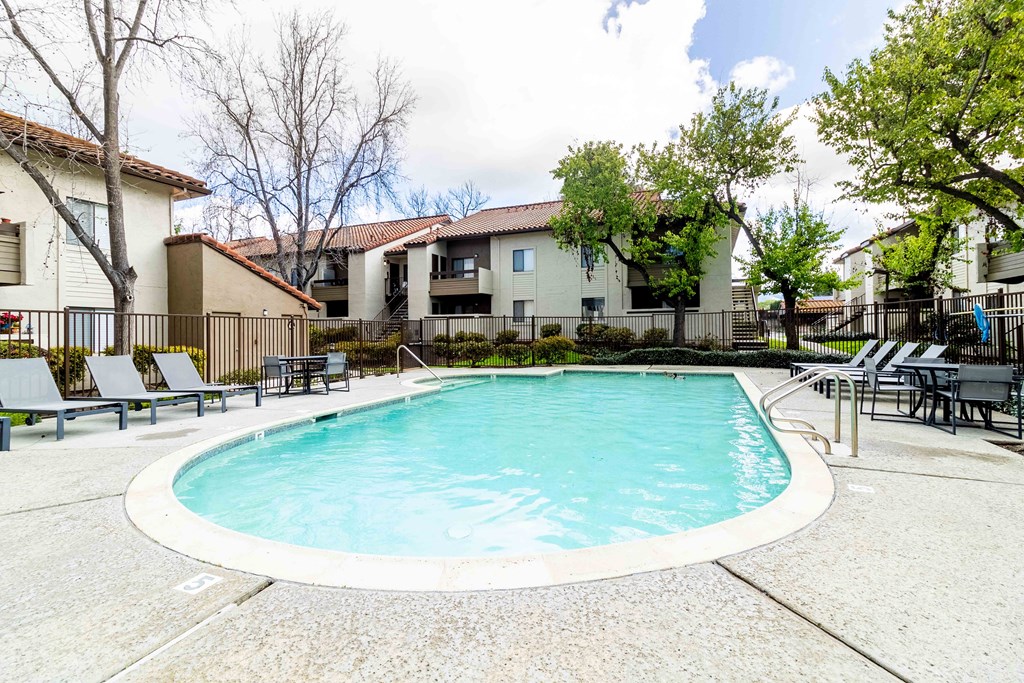 A swimming pool surrounded by lounge chairs and trees.