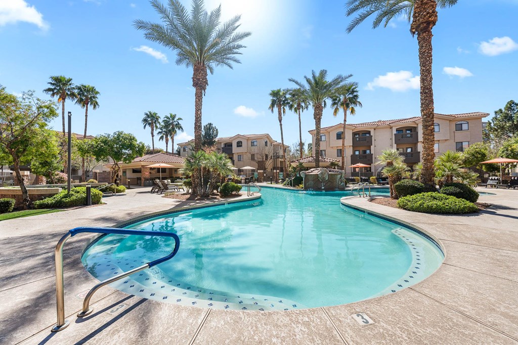 A large swimming pool surrounded by palm trees and apartment buildings.