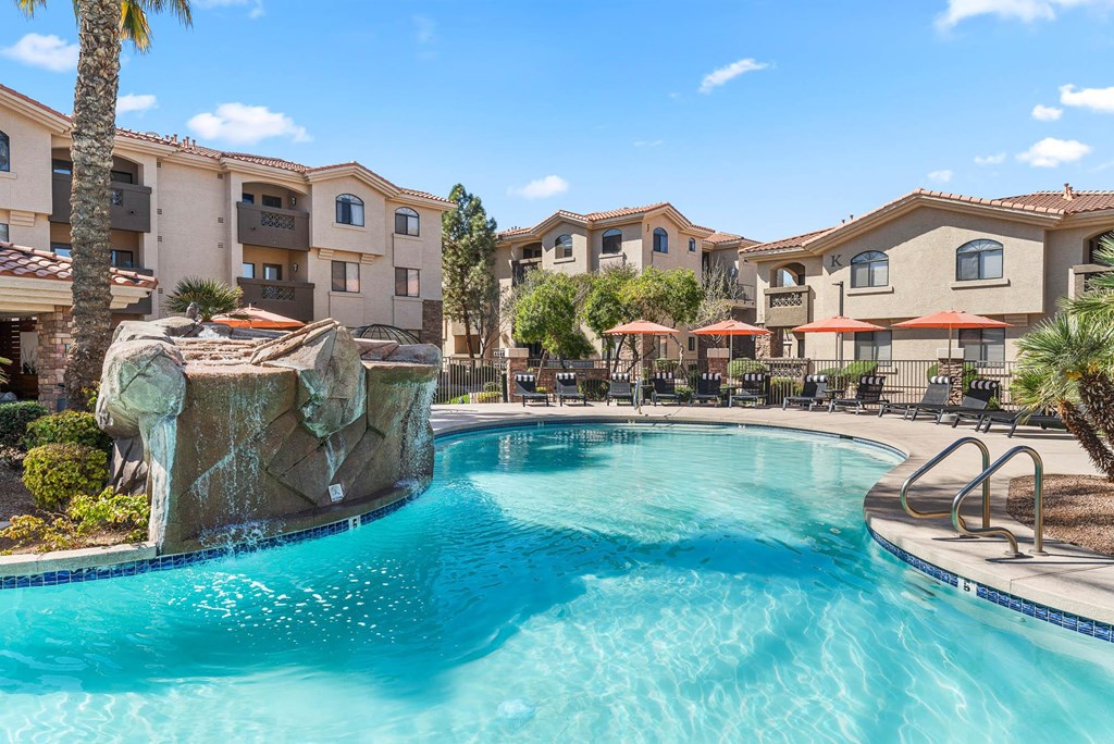 A swimming pool with a waterfall feature in front of apartment buildings.