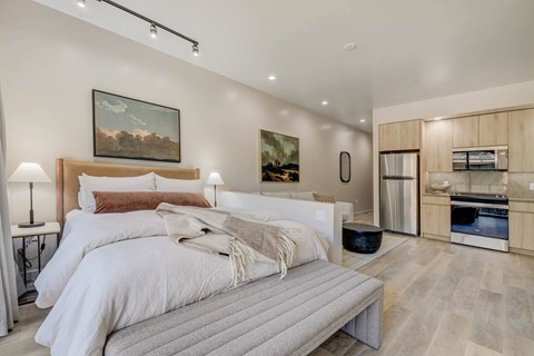 A bedroom with two beds and a kitchen area in the background.