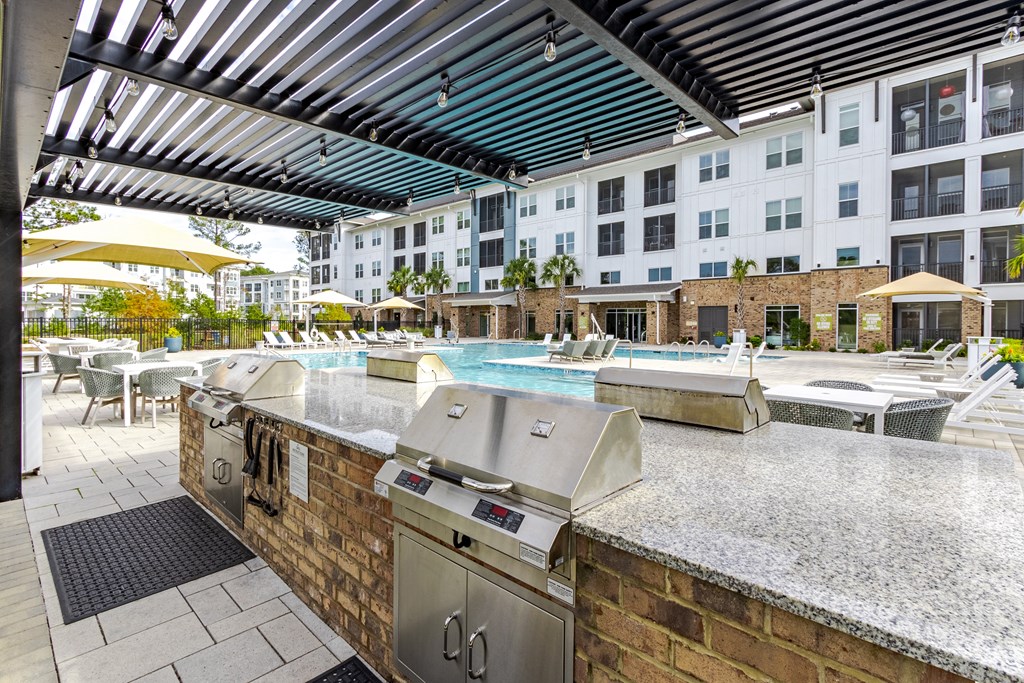 A barbecue grill is on a patio with a pool table and a building in the background.