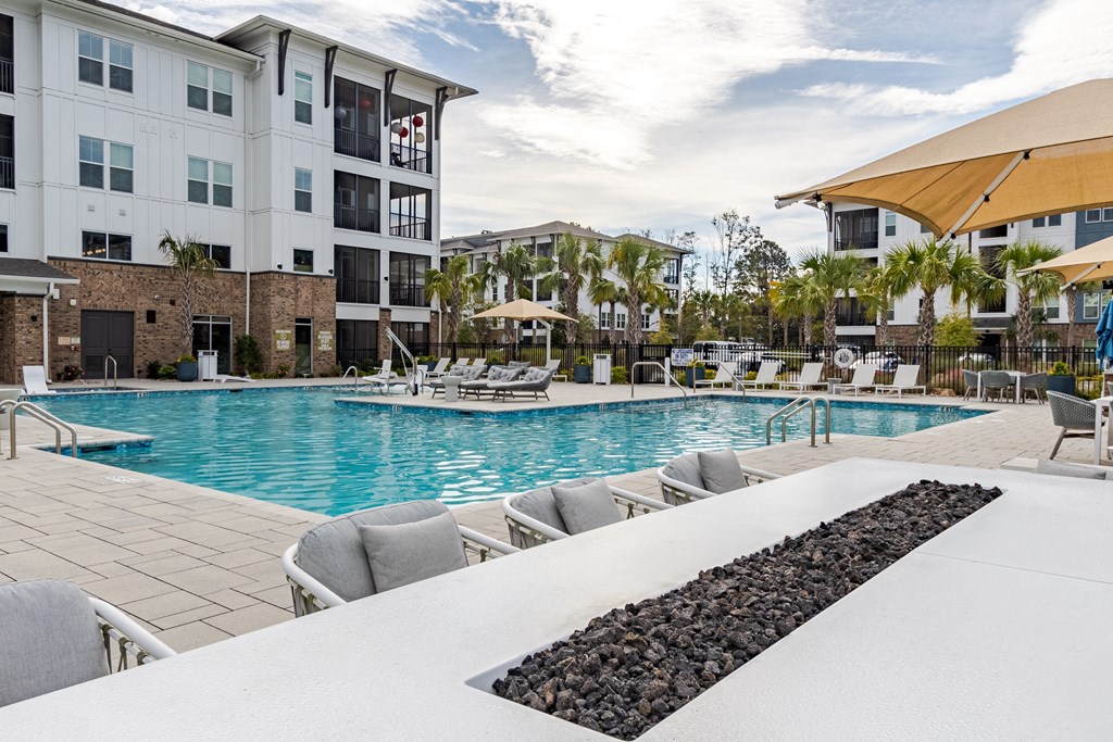 A large swimming pool with lounge chairs and a black rock border.