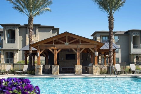A pool area with a wooden pavilion and palm trees.
