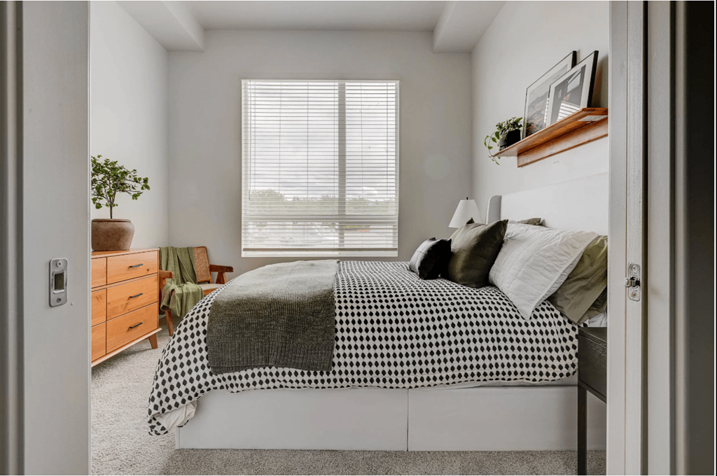 A bedroom with a bed, a dresser, and a window with blinds.