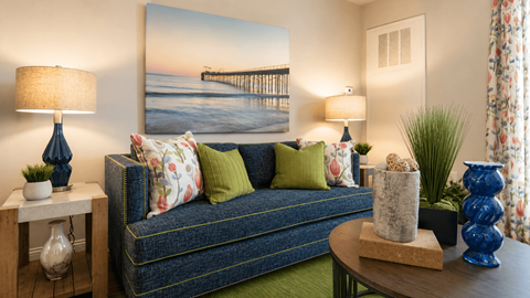 A living room with a couch, a table, and a painting of a pier on the wall.