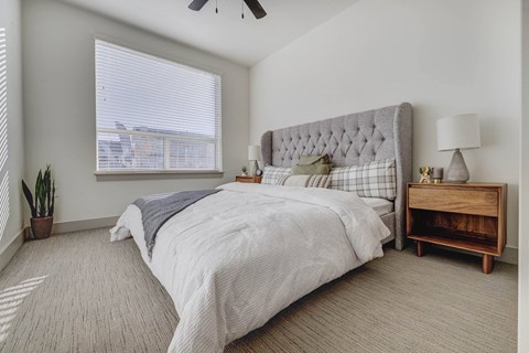 A spacious bedroom with a large bed and a wooden nightstand the room has large windows that provides a lot of natural light