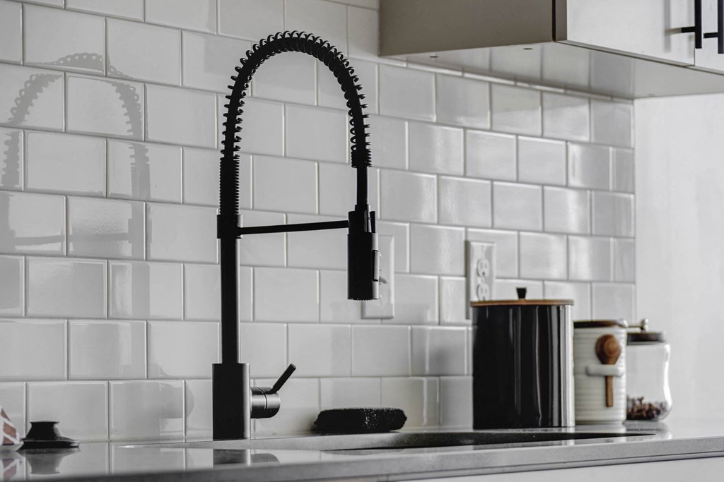 A kitchen sink with a black faucet and a white tile backsplash.