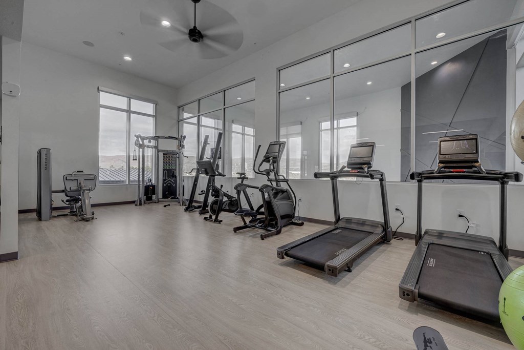 A spacious gym with treadmills, elliptical machines, and a fan.