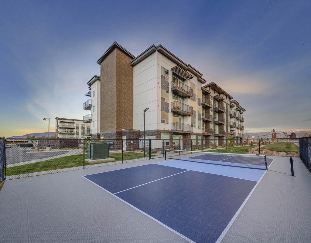 A tennis court is located in front of apartment buildings.