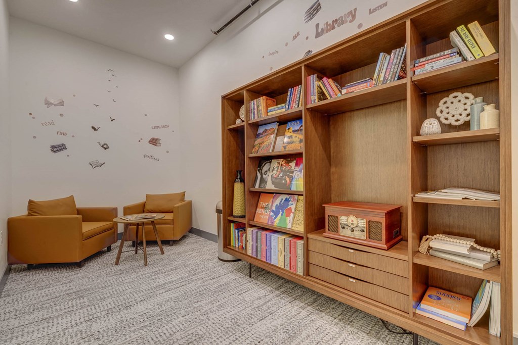 A room with a bookshelf, chairs, and a carpet.