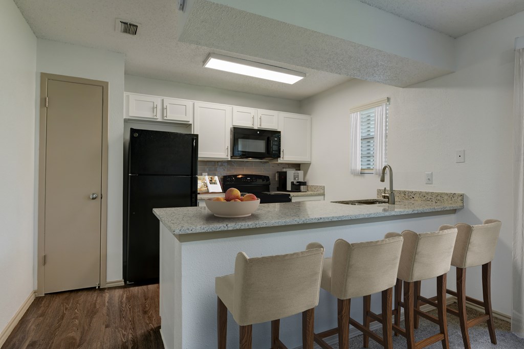 A kitchen with a black fridge, microwave, and a bowl of fruit on the counter.