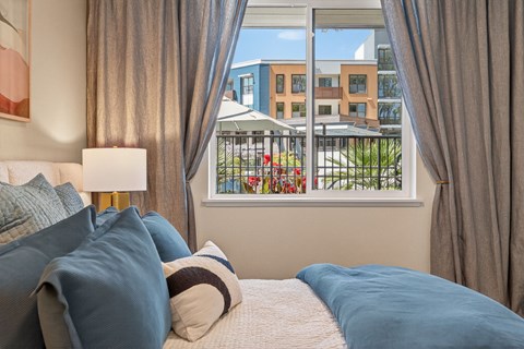 A bedroom with a large bed and a view of a balcony with a building in the background.