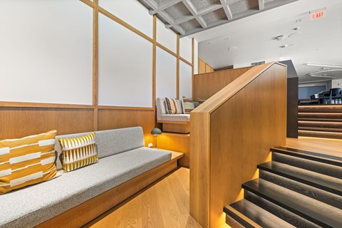 A staircase with a wooden banister and a grey carpeted bench with yellow and white striped pillows.
