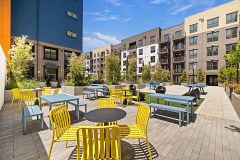 A patio with tables and chairs in front of apartment buildings.