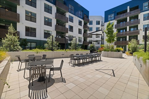 A patio with chairs and tables is surrounded by apartment buildings.
