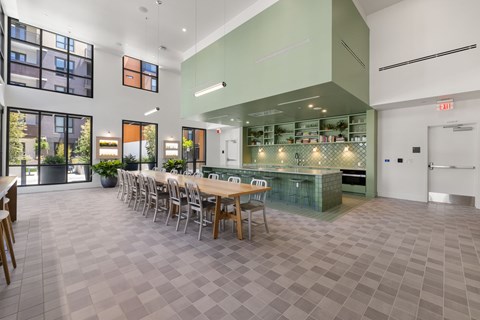 A long table is surrounded by chairs in a room with a green kitchen area.