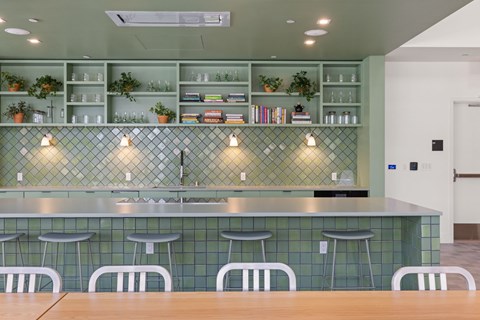 A modern bar with white stools and a green backdrop.