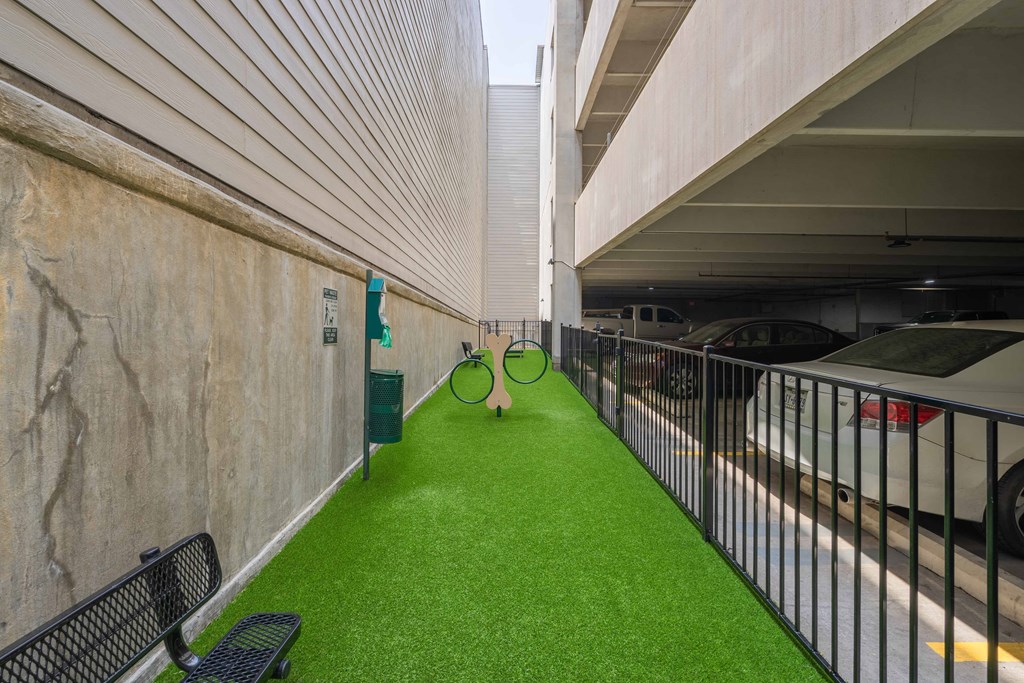 a pet yard with artificial turf and a bench in front of a parking garage
