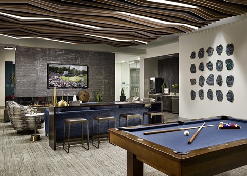 A pool table is in the middle of a room with a bar and a picture on the wall.