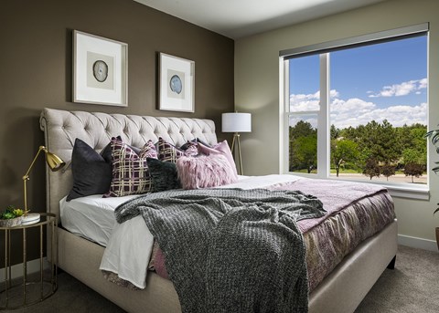 A bedroom with a large bed and a view of the outdoors through a large window.