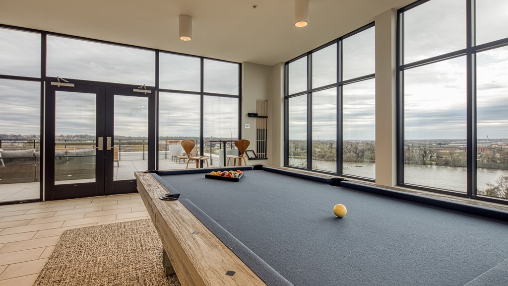 A pool table with a yellow ball on it in a room with large windows.