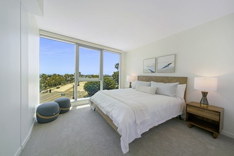 a bedroom with a large window and a bed with a white comforter