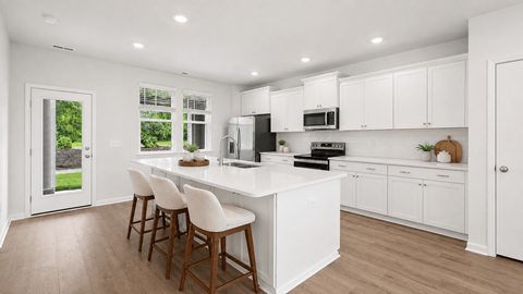 A kitchen with white cabinets and a white island with three bar stools.