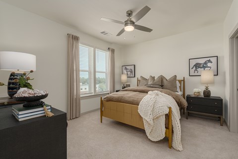 A bedroom with a bed, a ceiling fan, and a nightstand with a lamp.