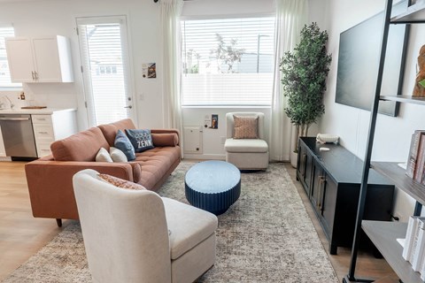 A living room with a brown couch, a blue ottoman, and a white chair.