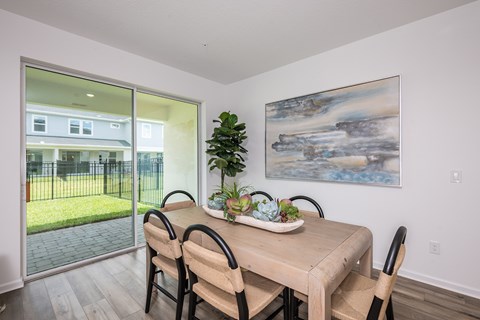 A dining room with a table and chairs and a painting on the wall.