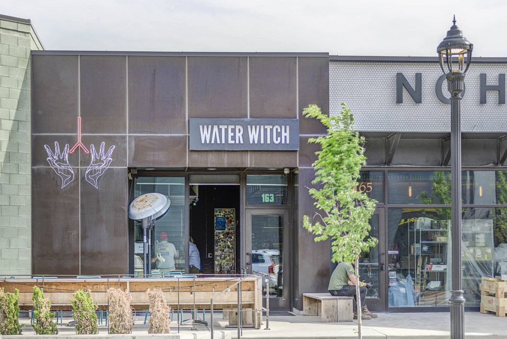 a man sitting on a bench in front of a building with a sign that reads water witch