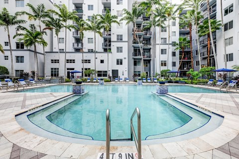 A swimming pool in front of a building with palm trees.