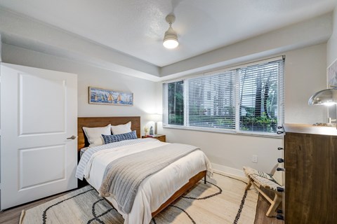 A bedroom with a bed, a bench, and a window with blinds.