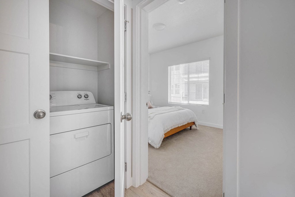 a laundry room with a washer and dryer and a bed in the background