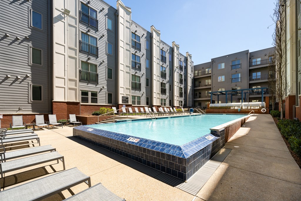 an outdoor pool with lounge chairs in front of an apartment building