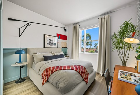A bedroom with a bed, a desk, and a window.