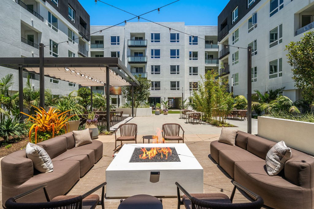 A patio with a fire pit and chairs is surrounded by buildings.