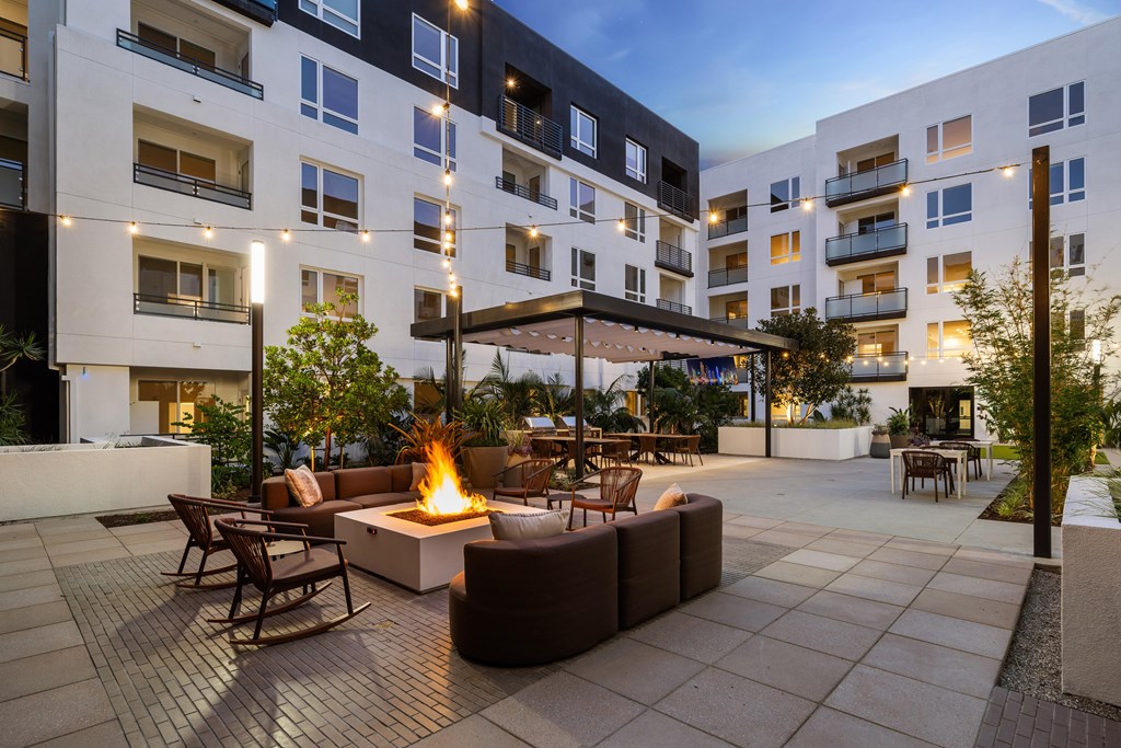 A patio with a fire pit and chairs is surrounded by apartment buildings.