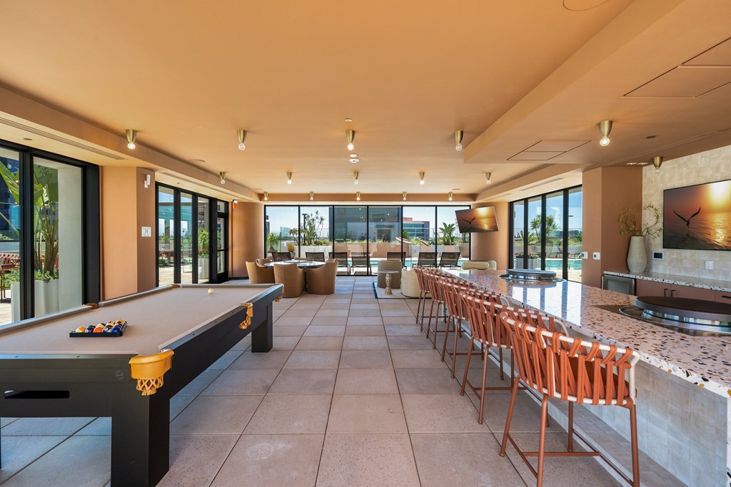 A billiard table is in the middle of a room with a bar and chairs.