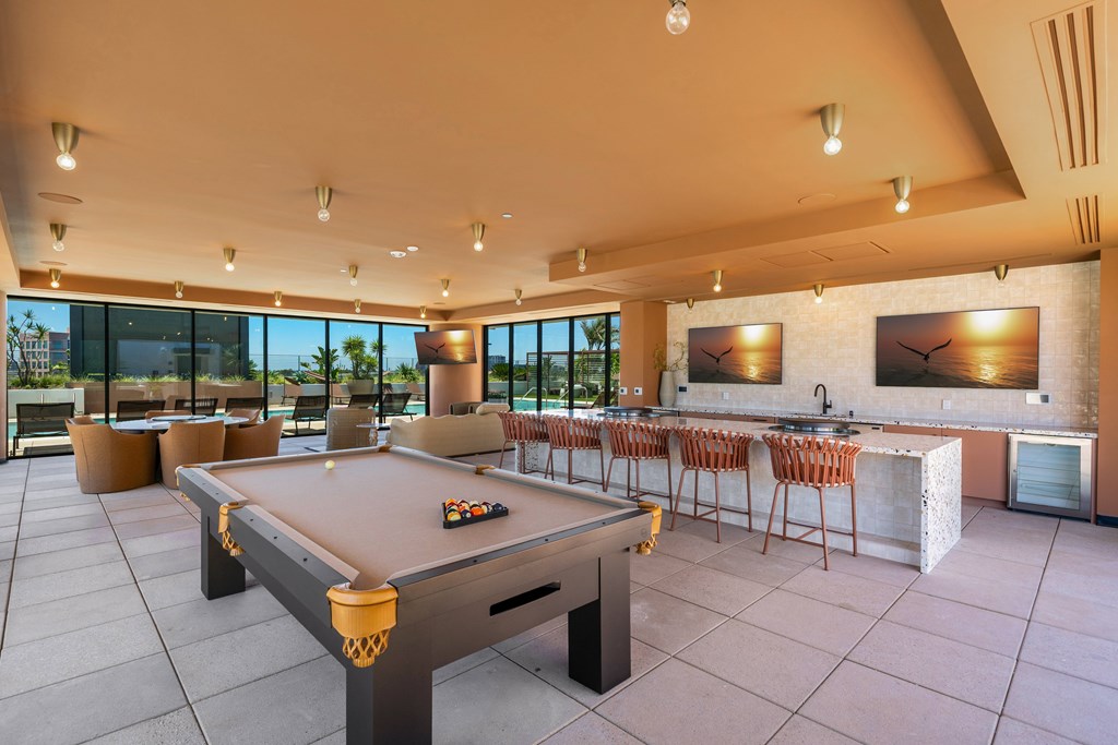 A pool table is in the middle of a room with a bar and chairs.
