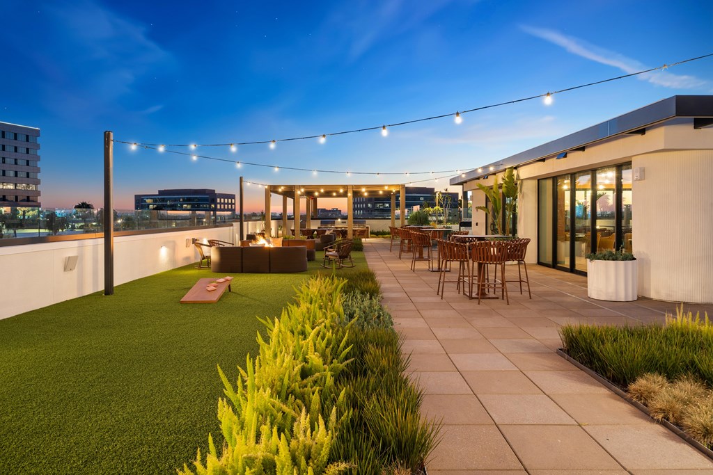 A rooftop patio with a table and chairs is illuminated by string lights.