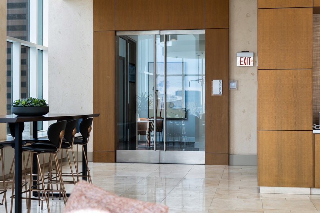 A modern dining area with a table and chairs, a glass door, and a white exit sign on the wall.