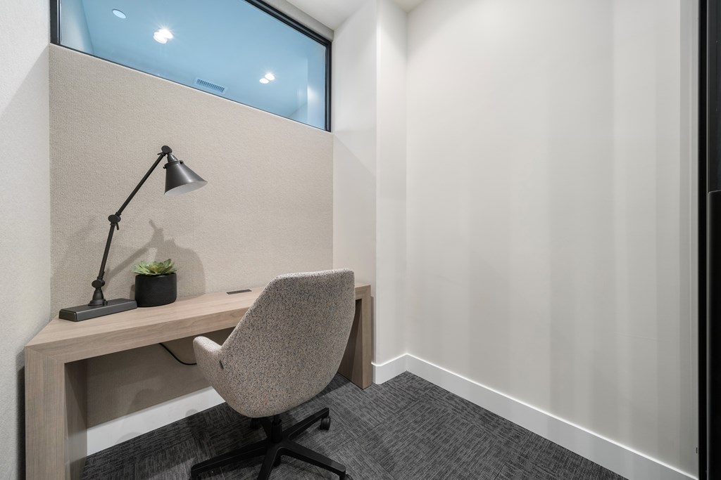 A grey chair is in front of a desk with a lamp and a plant on it.