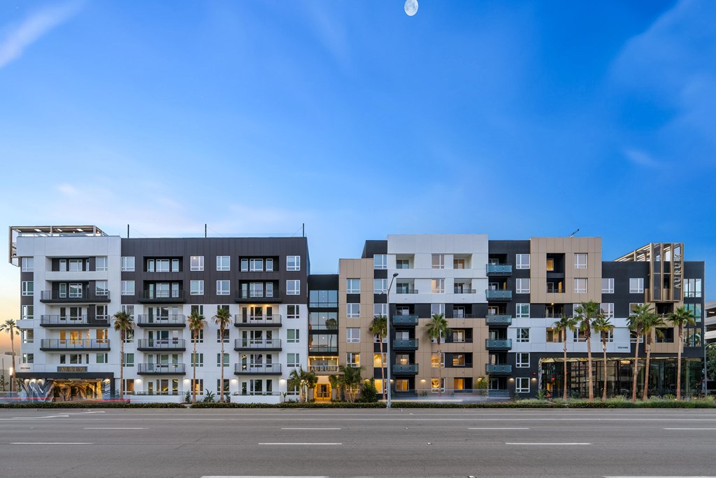 A row of modern apartment buildings with balconies and palm trees.