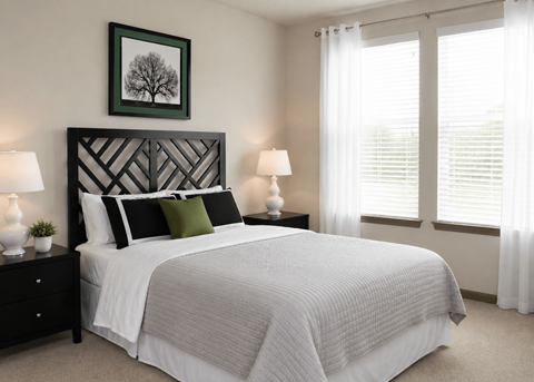 Spacious apartment bedroom featuring a large bed, bedside lamps, wall art, and ample natural light at Stone Pointe.