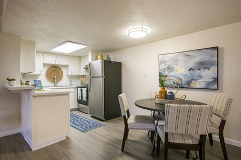 A kitchen with a refrigerator, sink, and a dining table with chairs.
