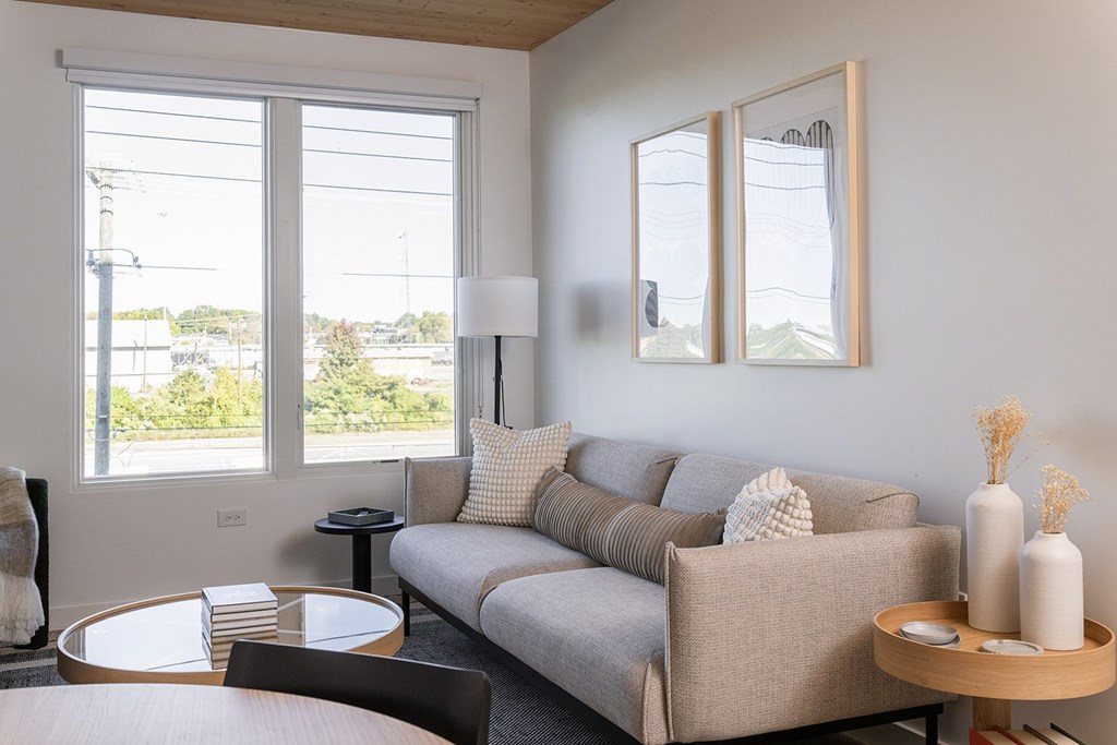 A living room with a grey couch, a round table, and a large window.