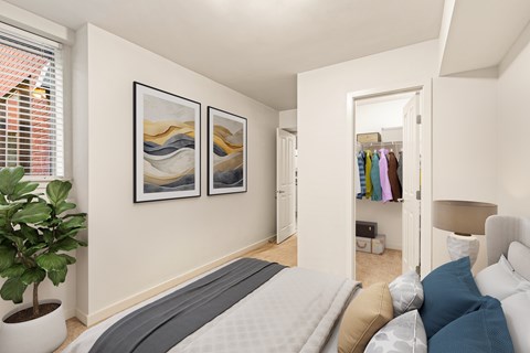 A bedroom with a bed, pillows, a plant, and two pictures on the wall.