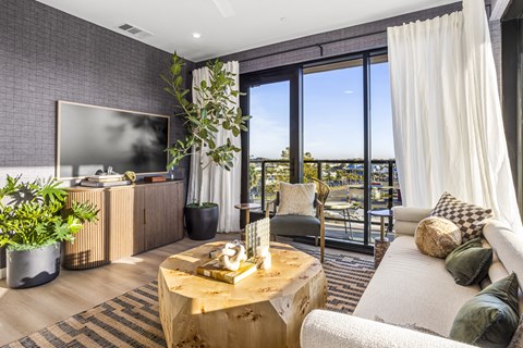 A living room with a flat screen TV, a coffee table, and a view of the city.