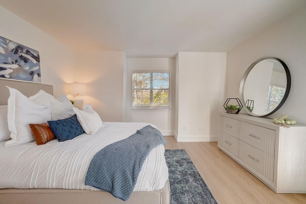 A bedroom with a large bed, a round mirror, and a window with a view of trees.